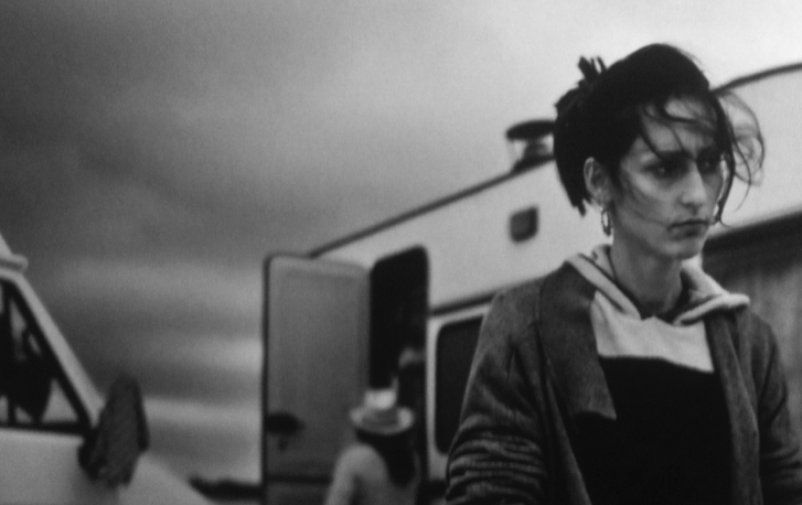 A frustrated looking Roma woman in front of a camper van. Everything's black and white.