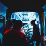 The open doors of an ambulance at night, with paramedics rushing a patient in.