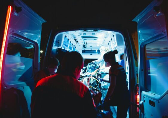 The open doors of an ambulance at night, with paramedics rushing a patient in.