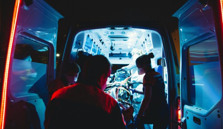 The open doors of an ambulance at night, with paramedics rushing a patient in.